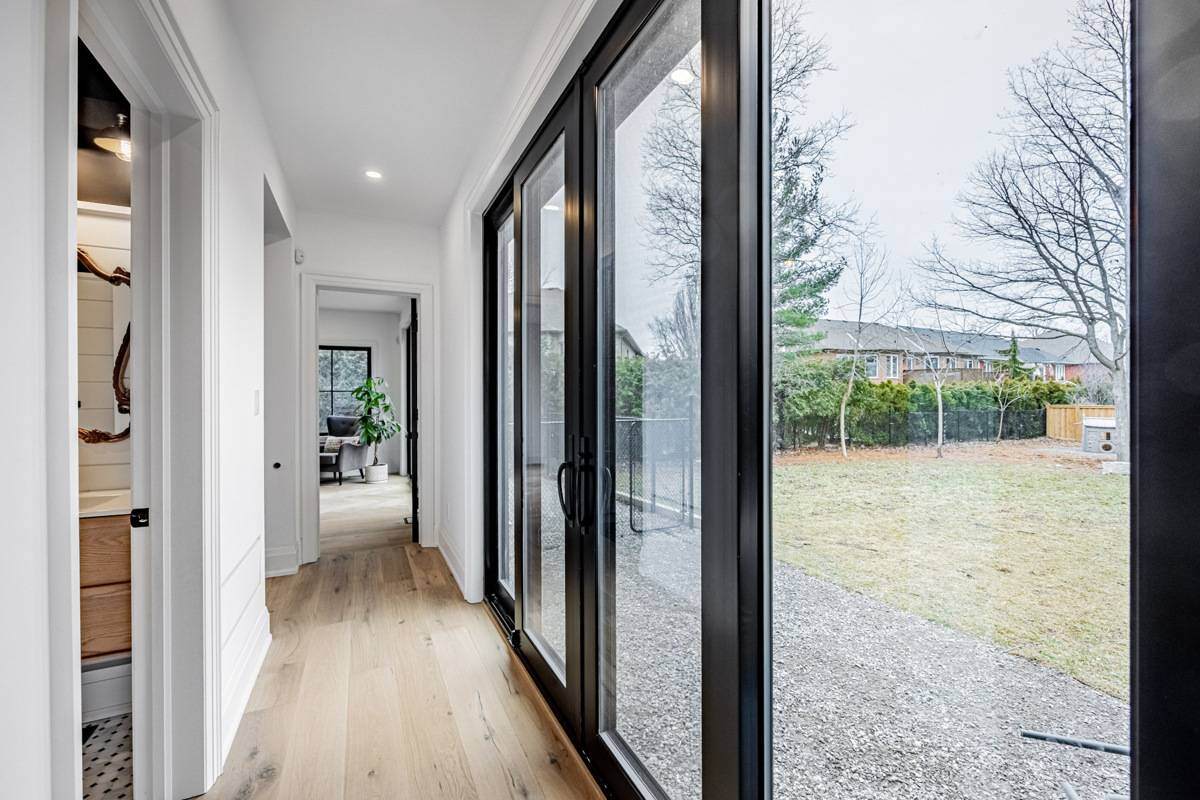 A hallway with floor-to-ceiling glass doors leading to a backyard, featuring natural light and wood flooring. | Ever After Homes