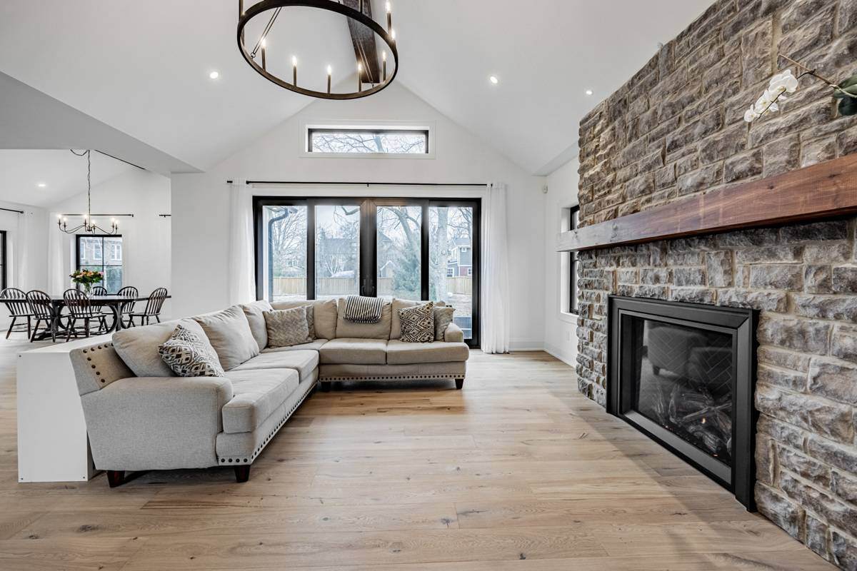 A bright living area with a sectional sofa, stone fireplace, and views of the dining and kitchen spaces in the background. Large windows and a vaulted ceiling with exposed beams enhance the airy feel. | Ever After Homes