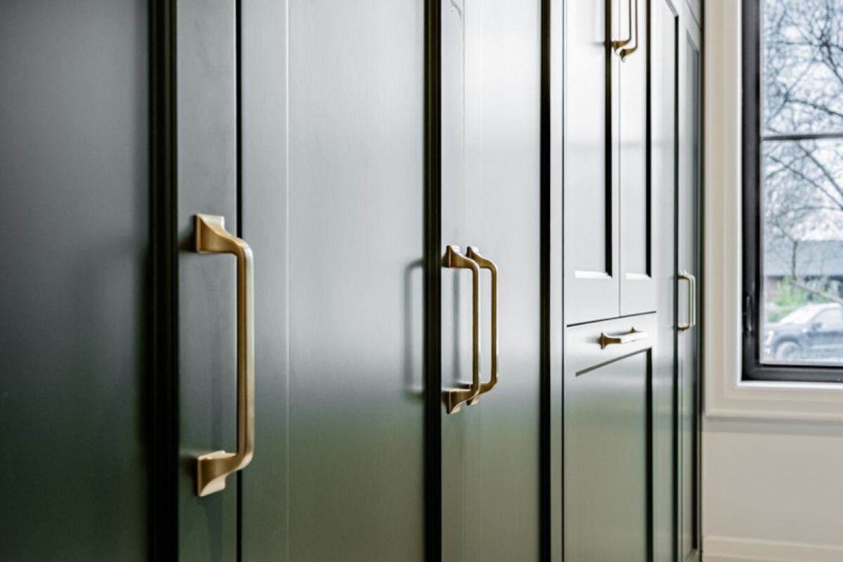 A close-up of deep green cabinetry with sleek brass handles, highlighted by natural light from a nearby window. | Ever After Homes